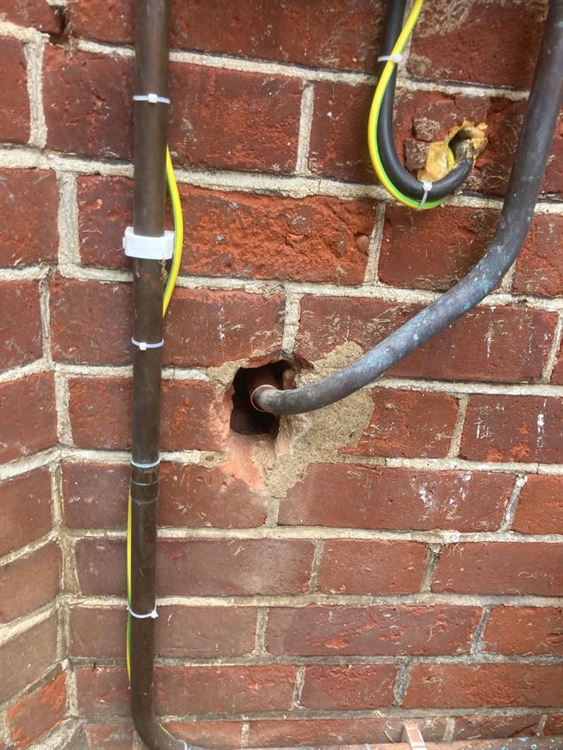 Gas pipework and green and yellow bonding conductor beside the exterior brick wall